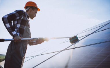 A worker wearing a hard hat performs solar panel cleaning in Los Angeles using a long-handled brush.