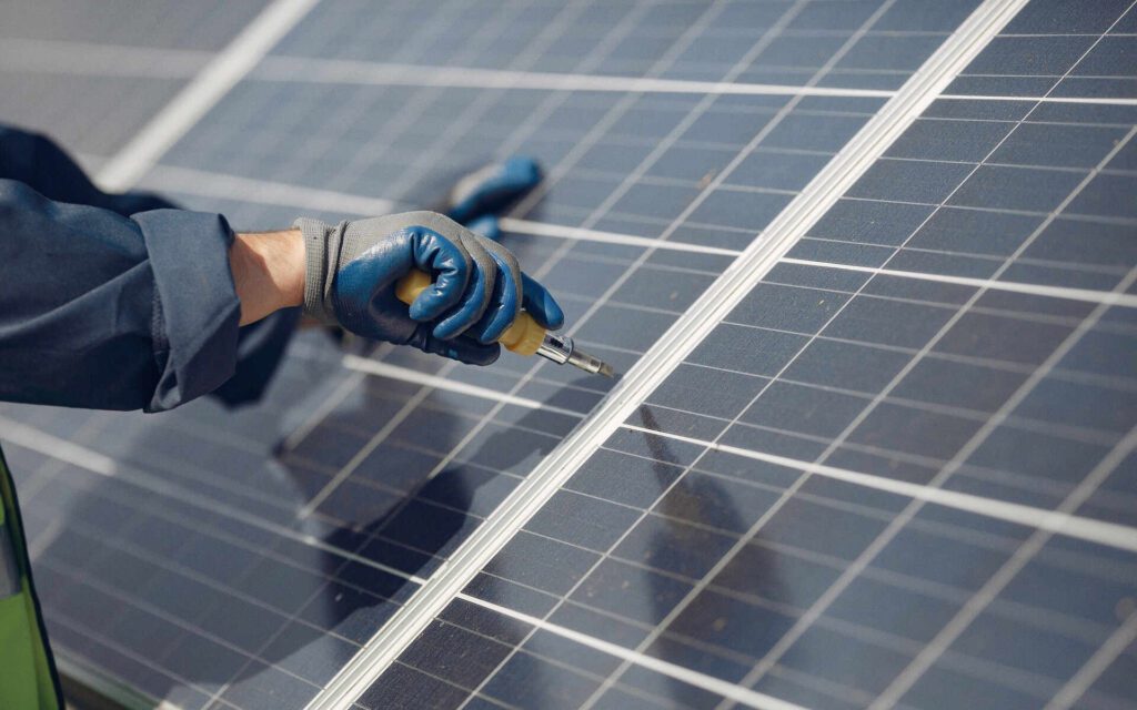 Technician wearing gloves performs solar panel cleaning with a specialized tool.