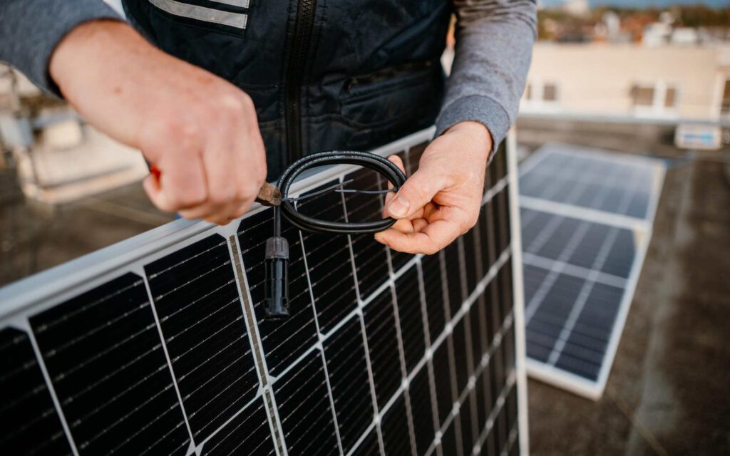 A technician performing solar panel maintenance by adjusting wiring on a rooftop solar panel.