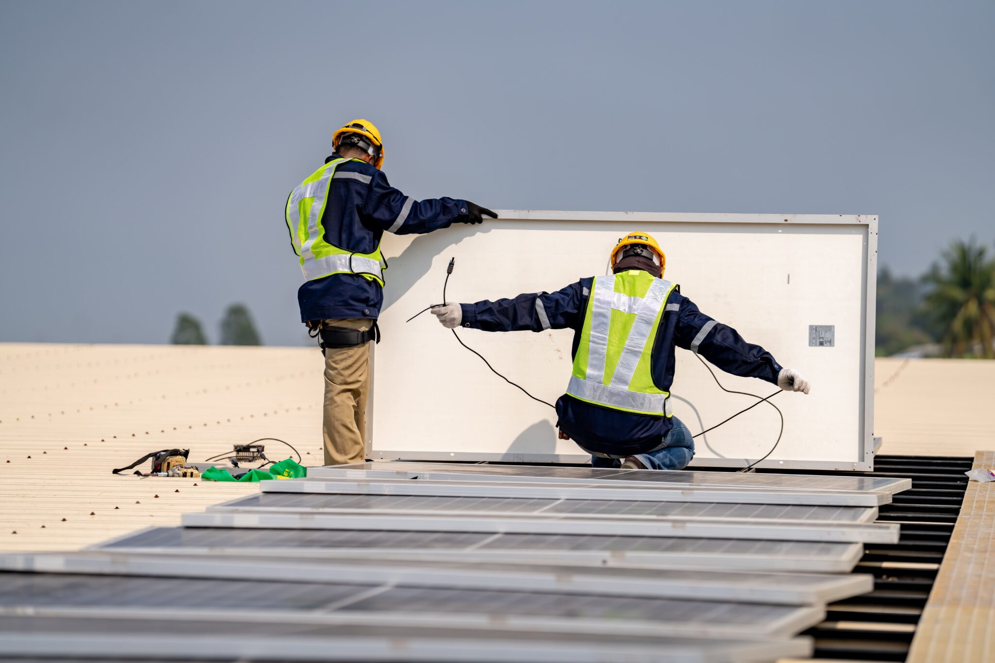 Two technicians perform solar panel maintenance on a rooftop by inspecting and adjusting the modules.