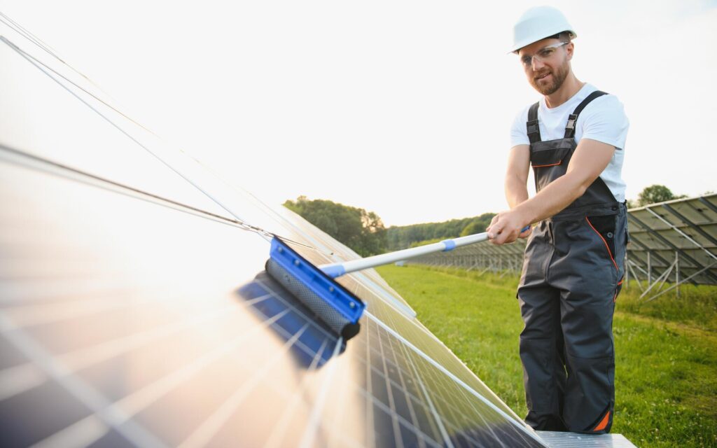 Worker performing solar panel cleaning with a brush tool on an outdoor solar array.
