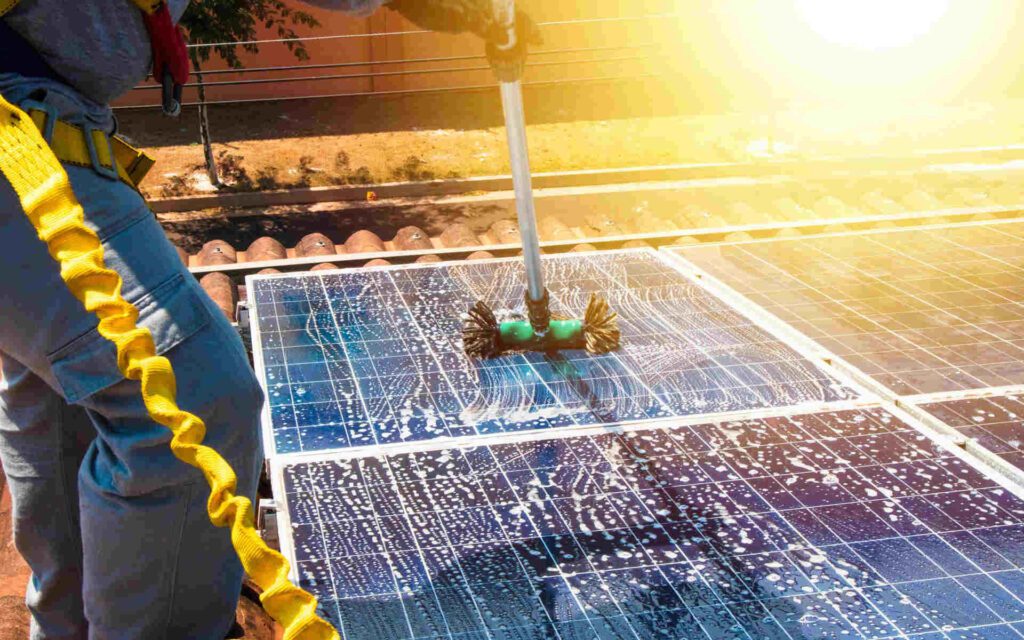 Worker performing solar panel cleaning services using a brush and water on rooftop panels.