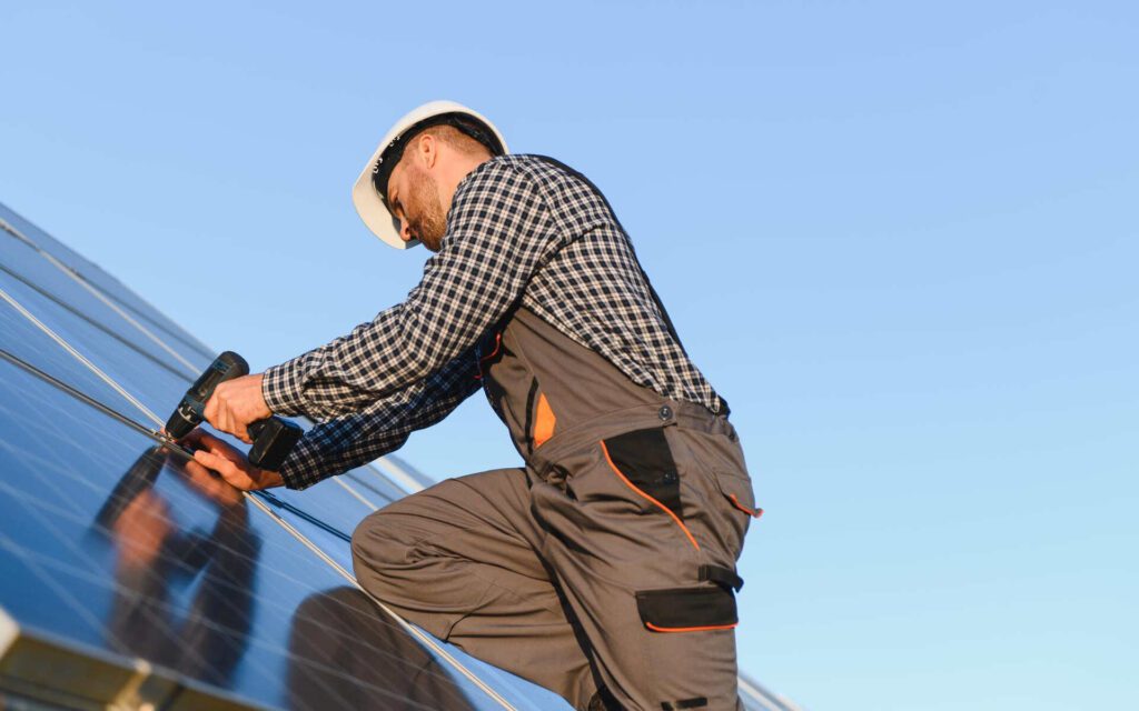 Technician performing solar roof leak repair while securing solar panels with a drill.