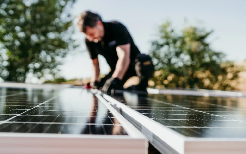 A technician performs coastal solar system maintenance by working on rooftop solar panels under sunny weather.