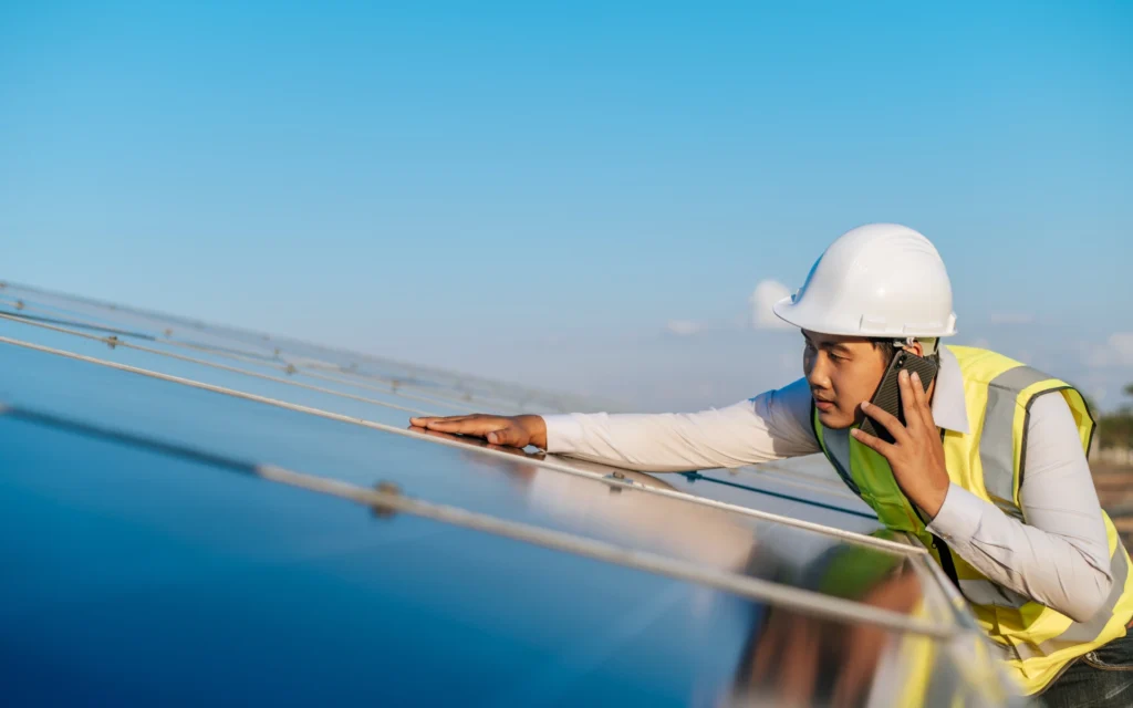 A technician inspects solar panels while speaking on the phone, illustrating renewable energy work in Pacific Palisades.