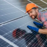 Technician in a hard hat inspecting solar panels on a rooftop, illustrating coastal weather impact on solar panels.