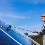 A technician wearing a hard hat cleaning rooftop solar panels as part of solar panel maintenance in Pasadena, CA.