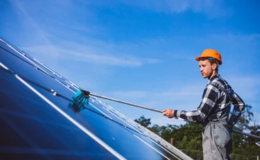 A technician wearing a hard hat cleaning rooftop solar panels as part of solar panel maintenance in Pasadena, CA.