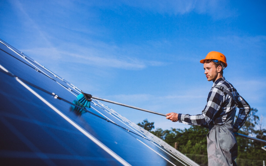 A technician wearing a hard hat cleaning rooftop solar panels as part of solar panel maintenance in Pasadena, CA.