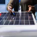 A professional pointing at a solar panel during a team discussion about Power on BH in a technical workspace.