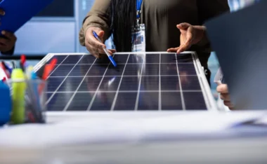 A professional pointing at a solar panel during a team discussion about Power on BH in a technical workspace.